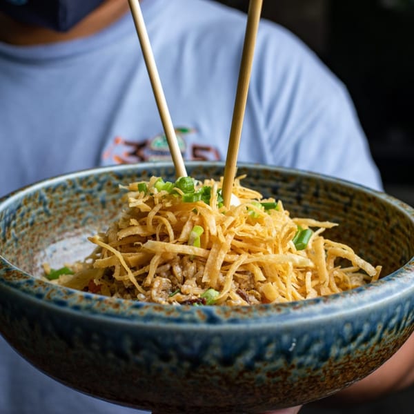 Peruvian chaufa rice dish with crispy noodles and green onions, held by a person with chopsticks.