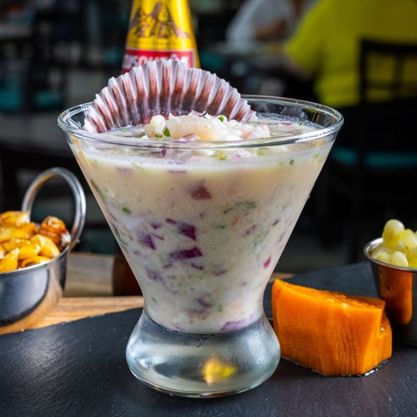 Peruvian leche de tigre ceviche in a martini glass with a scallop shell, corn, and sweet potato.