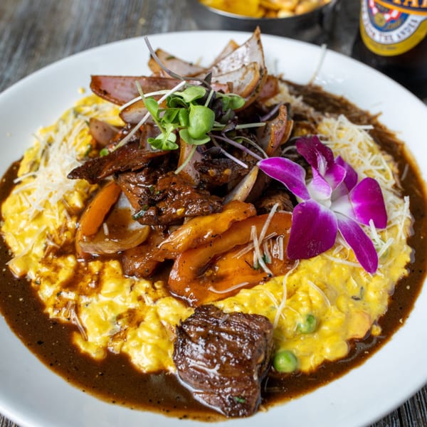 Peruvian Lomo Saltado with beef, onions, peppers, and microgreens, served over yellow risotto with a purple orchid.