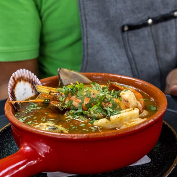 Peruvian seafood stew in a red pot, garnished with cilantro, shrimp, squid, and a scallop shell.