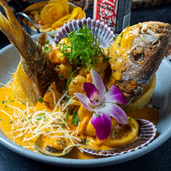 Peruvian fried fish with seafood in orange sauce, garnished with an orchid and shredded cheese.