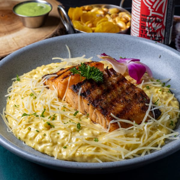 Grilled salmon over yellow Peruvian risotto, topped with shredded cheese and a purple orchid.