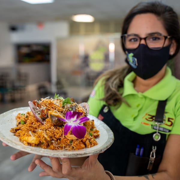 A 305 Peruvian Modern Cuisine server holds a plate of Peruvian seafood rice with a purple orchid.