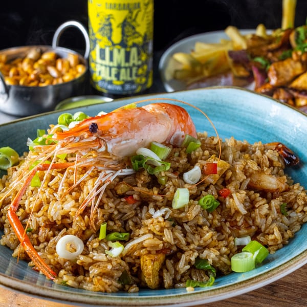 Peruvian chaufa rice with a large shrimp, green onions, and a beer in the background.