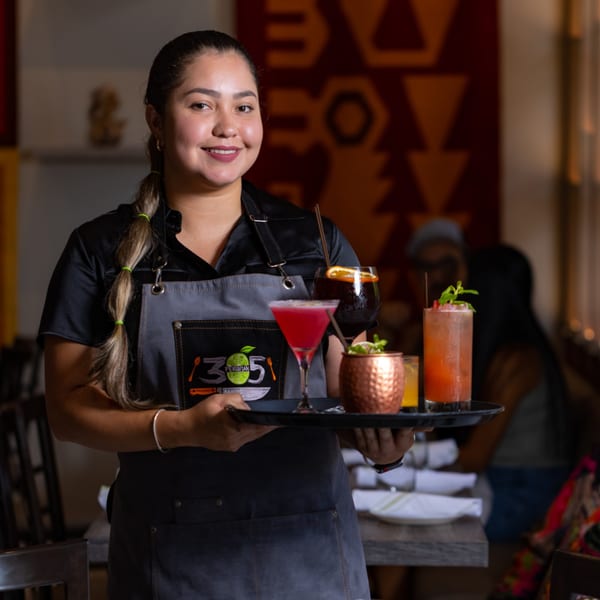 Smiling 305 Peruvian Modern Cuisine server holding a tray with four colorful cocktails.